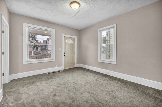 carpeted entrance foyer featuring visible vents, a textured ceiling, and baseboards