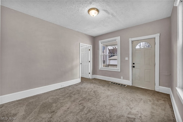 entryway featuring a textured ceiling, carpet, visible vents, and baseboards