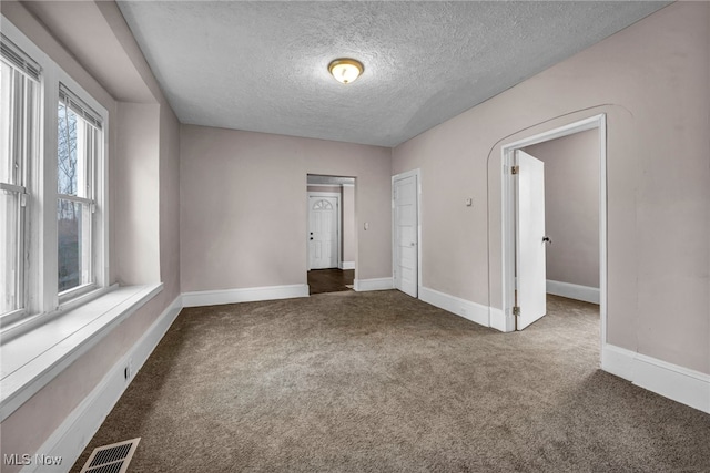 empty room featuring a textured ceiling, carpet, visible vents, and baseboards