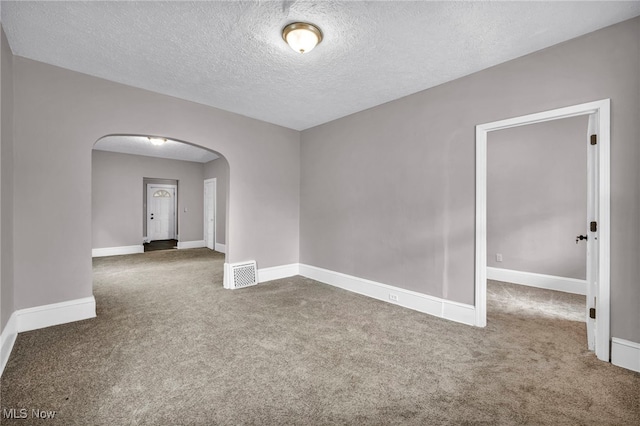 empty room featuring arched walkways, a textured ceiling, carpet flooring, visible vents, and baseboards