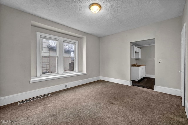 unfurnished room with visible vents, dark carpet, a textured ceiling, and baseboards