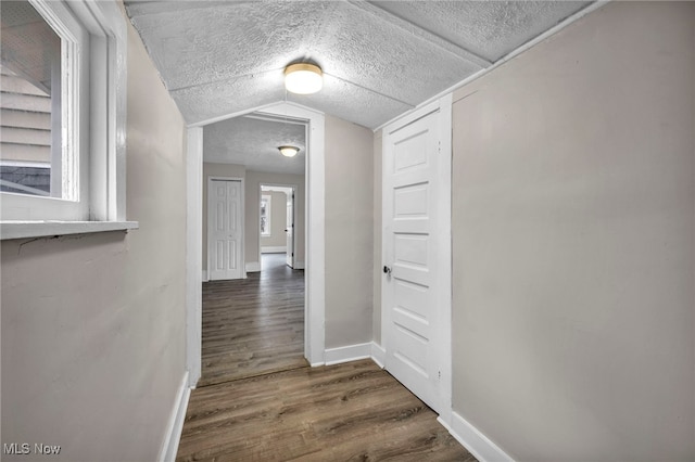 corridor featuring a textured ceiling, baseboards, vaulted ceiling, and wood finished floors