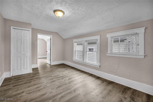 interior space featuring vaulted ceiling, a textured ceiling, baseboards, and wood finished floors