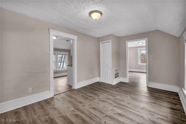 empty room featuring a textured ceiling, vaulted ceiling, wood finished floors, and baseboards