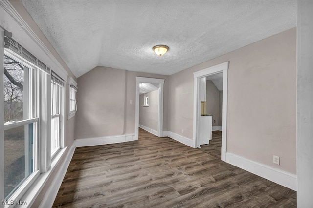 empty room with lofted ceiling, a textured ceiling, baseboards, and wood finished floors