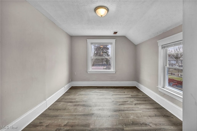 spare room featuring a textured ceiling, baseboards, dark wood finished floors, and a wealth of natural light