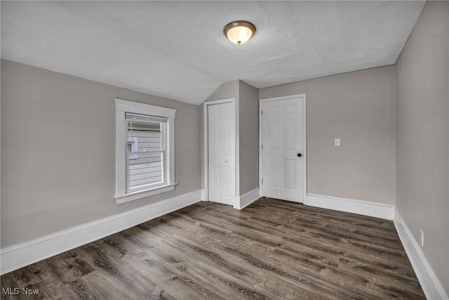 unfurnished bedroom featuring a textured ceiling, wood finished floors, baseboards, vaulted ceiling, and a closet