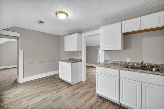 kitchen featuring visible vents, light wood-style flooring, white cabinetry, a sink, and a textured ceiling