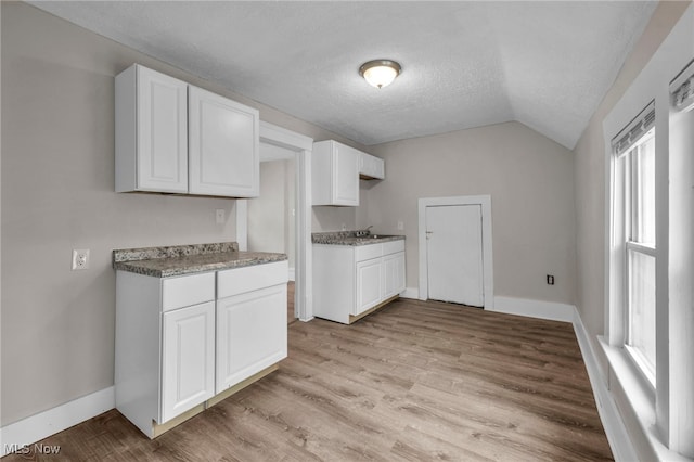 kitchen with lofted ceiling, a textured ceiling, baseboards, white cabinets, and light wood finished floors