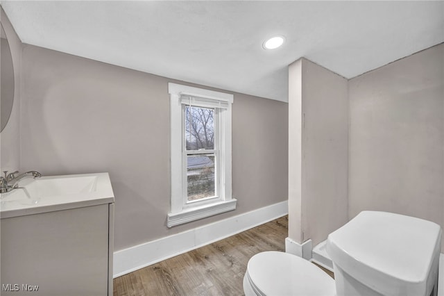 half bath featuring toilet, recessed lighting, wood finished floors, vanity, and baseboards