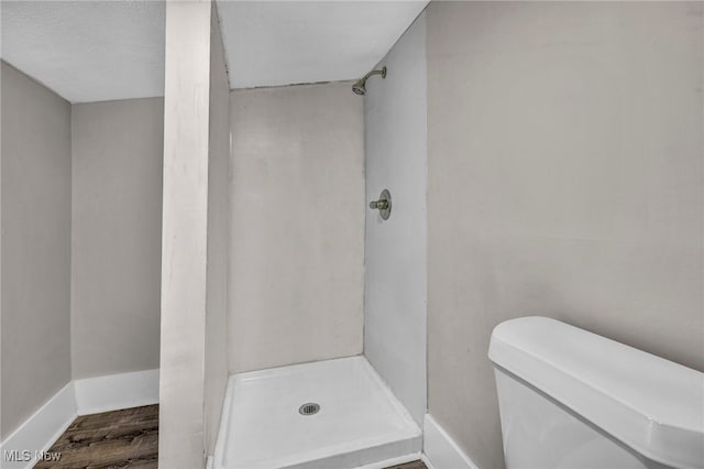 bathroom with wood finished floors, a shower stall, toilet, and baseboards