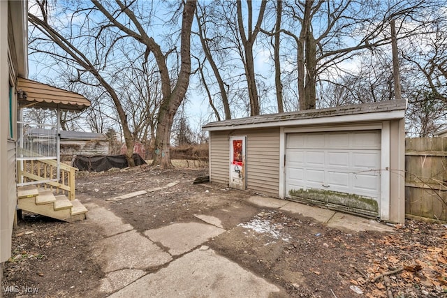 detached garage featuring concrete driveway and fence