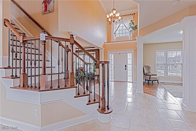 entrance foyer featuring a chandelier, a high ceiling, stairs, ornate columns, and crown molding