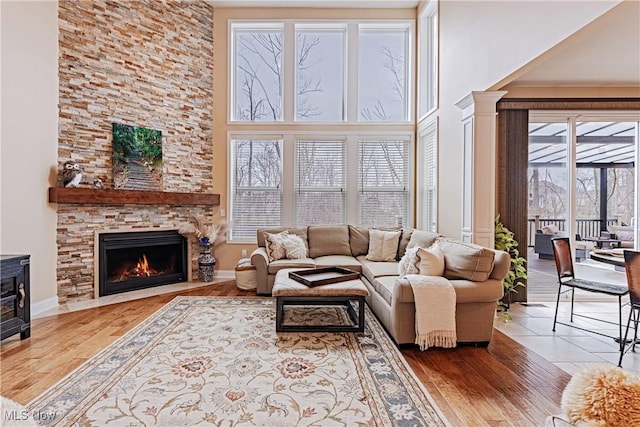 living room with a stone fireplace, a towering ceiling, and wood finished floors