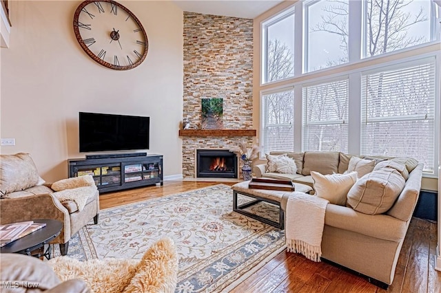 living area featuring a stone fireplace, a high ceiling, and hardwood / wood-style flooring