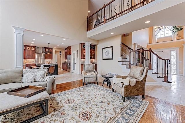 living area featuring a high ceiling, light wood-style floors, stairs, baseboards, and ornate columns