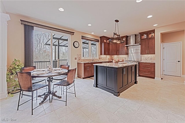 kitchen with wall chimney exhaust hood, backsplash, glass insert cabinets, and light stone countertops