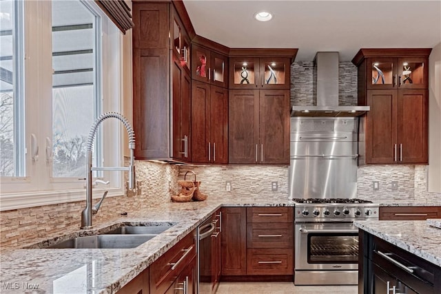 kitchen featuring light stone counters, a sink, wall chimney range hood, high end stainless steel range oven, and backsplash