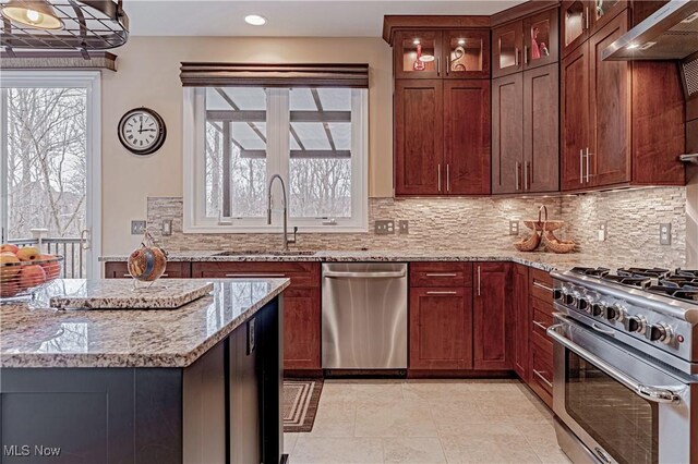 kitchen with light stone counters, stainless steel appliances, a sink, tasteful backsplash, and glass insert cabinets