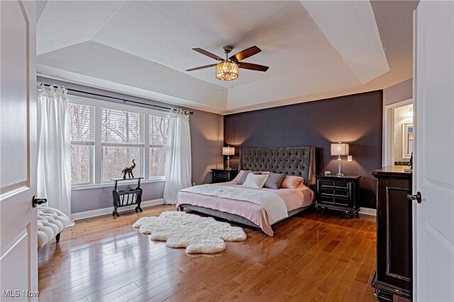 bedroom featuring a tray ceiling, wood finished floors, a ceiling fan, and baseboards