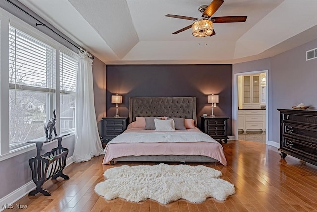 bedroom with visible vents, baseboards, a raised ceiling, and wood finished floors