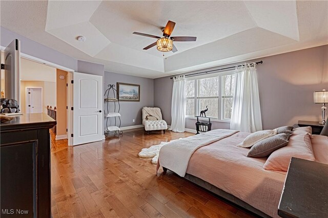 bedroom featuring a tray ceiling, a ceiling fan, hardwood / wood-style floors, and baseboards