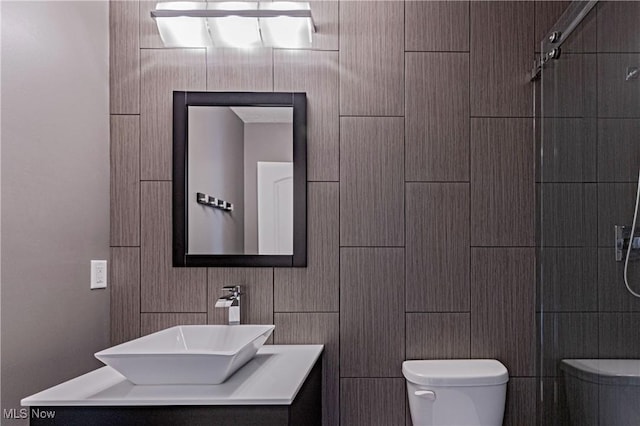 bathroom with tile walls, tiled shower, vanity, and toilet