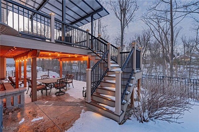 snow covered patio featuring stairway, outdoor dining area, and a pergola