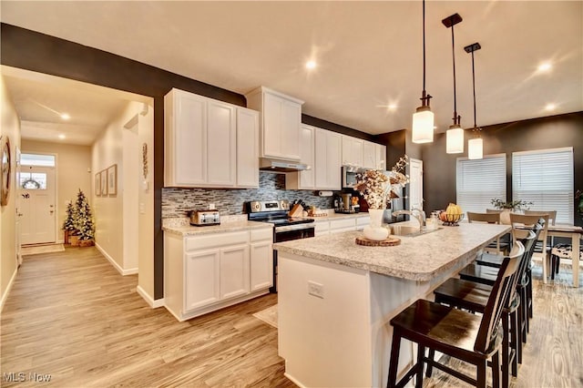 kitchen featuring a center island with sink, appliances with stainless steel finishes, light wood-style flooring, and under cabinet range hood