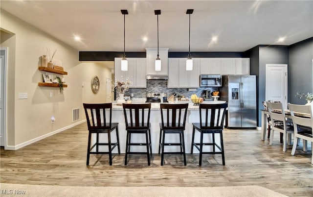 kitchen featuring light wood-type flooring, a kitchen breakfast bar, backsplash, stainless steel appliances, and white cabinets