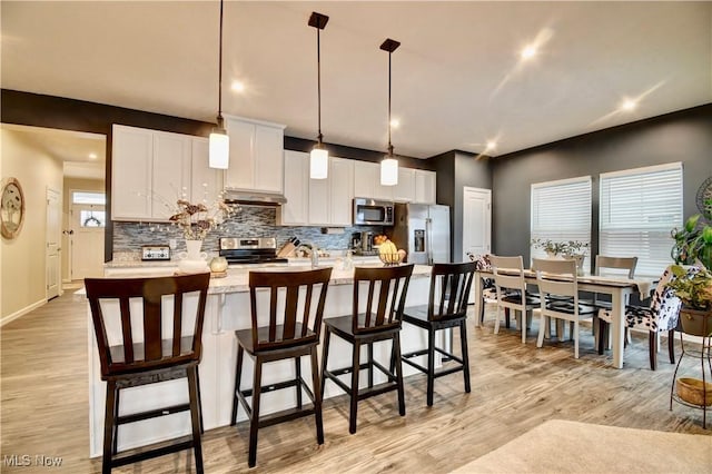 kitchen featuring under cabinet range hood, backsplash, a center island with sink, and appliances with stainless steel finishes