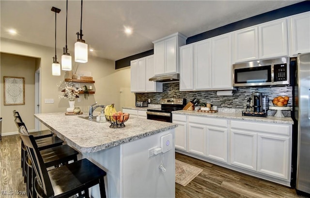 kitchen featuring under cabinet range hood, light countertops, decorative backsplash, dark wood-style floors, and stainless steel appliances