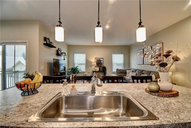 kitchen featuring a sink, light stone counters, open floor plan, and hanging light fixtures