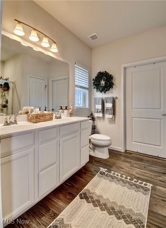 bathroom with visible vents, toilet, double vanity, wood finished floors, and a sink