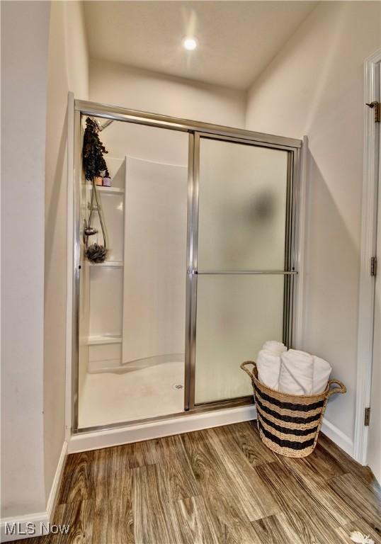 full bath featuring a stall shower, baseboards, and wood finished floors