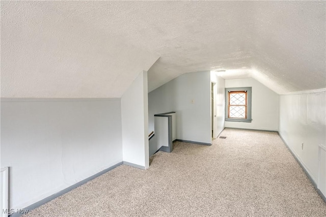 additional living space featuring a textured ceiling, carpet floors, vaulted ceiling, and baseboards