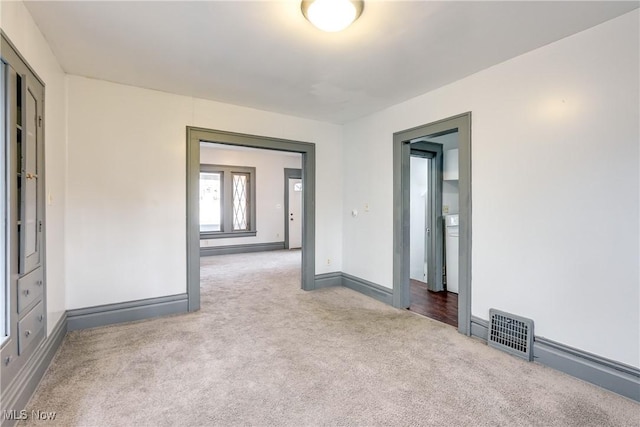 carpeted spare room with washer / dryer, visible vents, and baseboards