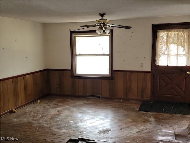 foyer featuring wooden walls, a wainscoted wall, a ceiling fan, visible vents, and wood-type flooring