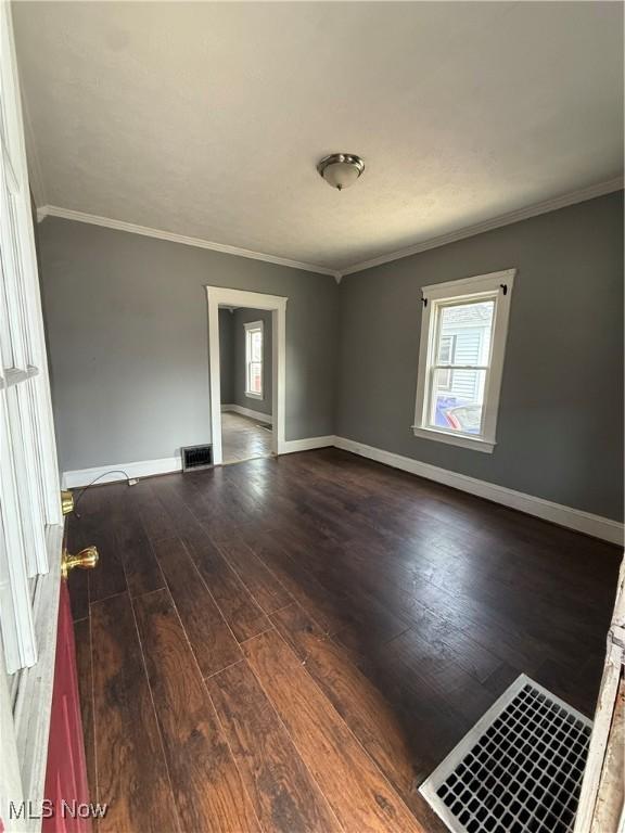 empty room featuring ornamental molding, a wealth of natural light, and wood finished floors