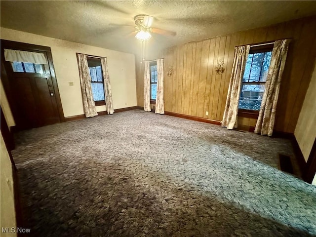 unfurnished bedroom featuring a textured ceiling, ceiling fan, wood walls, baseboards, and carpet