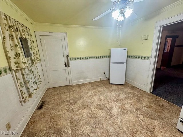 unfurnished room with visible vents, a wainscoted wall, ceiling fan, ornamental molding, and tile walls