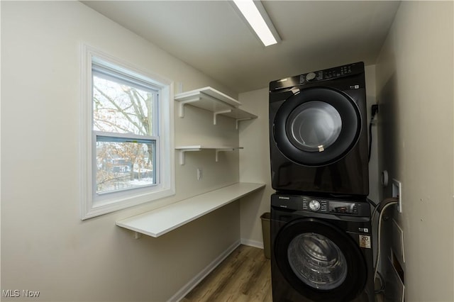 laundry area featuring laundry area, stacked washing maching and dryer, baseboards, and wood finished floors