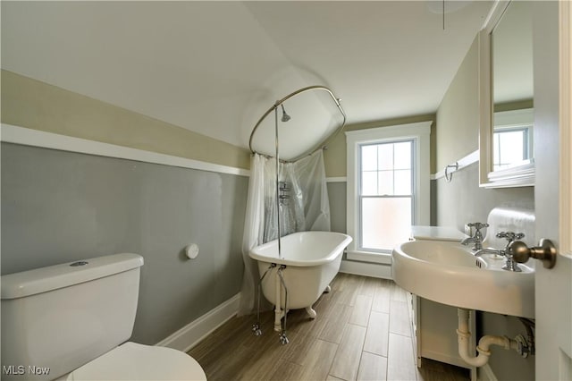 bathroom with a freestanding bath, toilet, wood finished floors, a shower with curtain, and baseboards