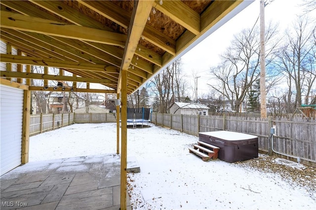 snowy yard with a patio, a trampoline, a fenced backyard, and a hot tub