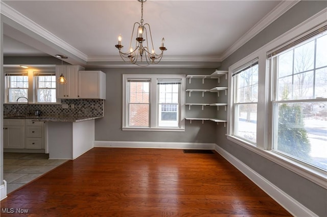 unfurnished dining area with baseboards, a healthy amount of sunlight, a sink, and crown molding