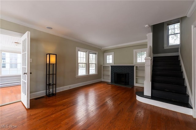 unfurnished living room with hardwood / wood-style flooring, a wealth of natural light, visible vents, ornamental molding, and stairs