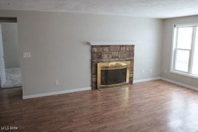 unfurnished living room featuring baseboards, wood finished floors, and a stone fireplace