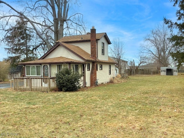 view of side of property featuring a lawn, a chimney, fence, a deck, and an outdoor structure