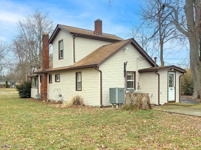 rear view of house featuring a chimney, a lawn, and roof with shingles