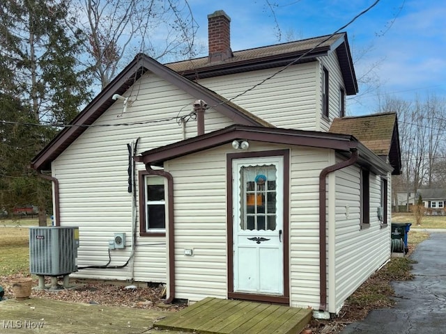 back of house featuring central AC unit, roof with shingles, and a chimney